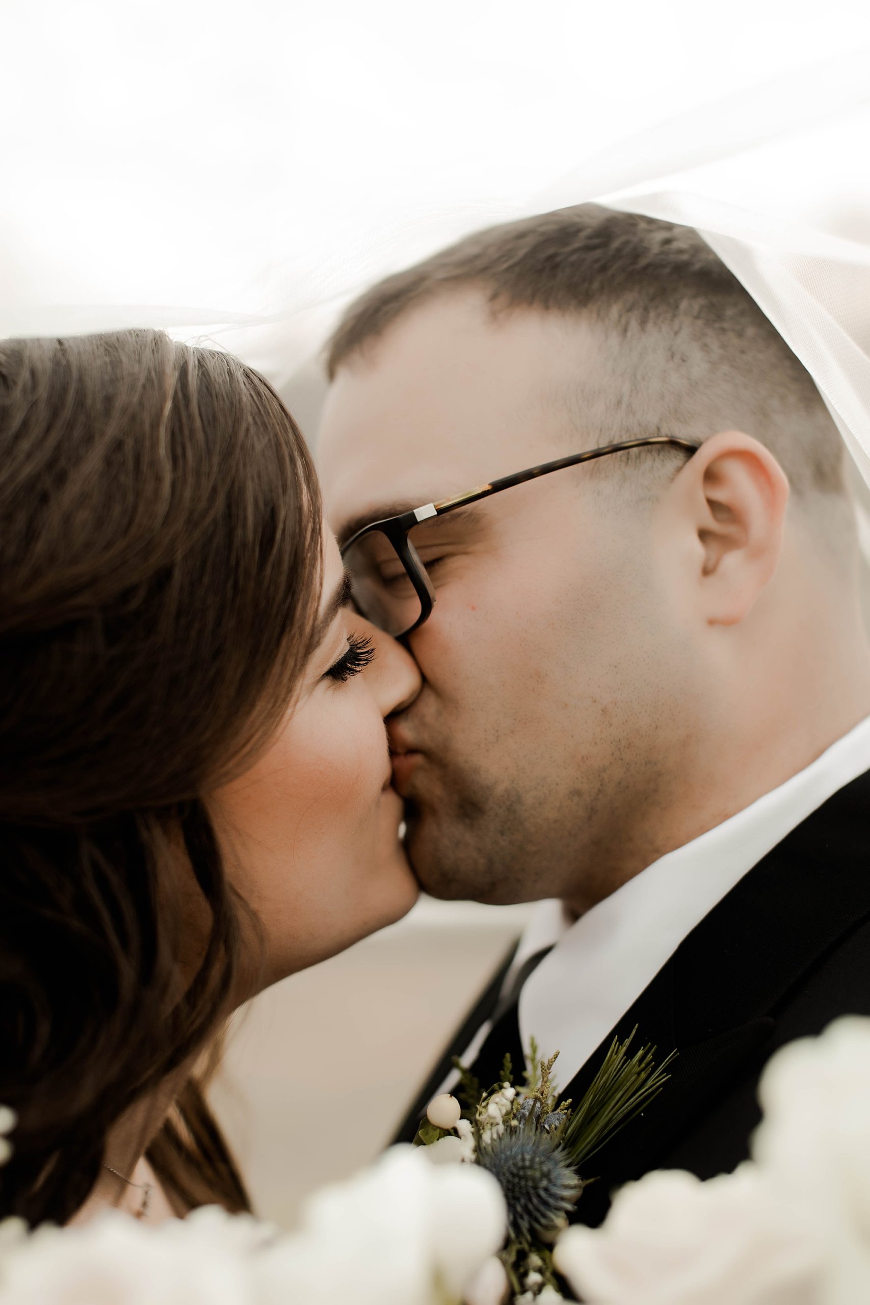 bride and groom kissing under wedding veil 